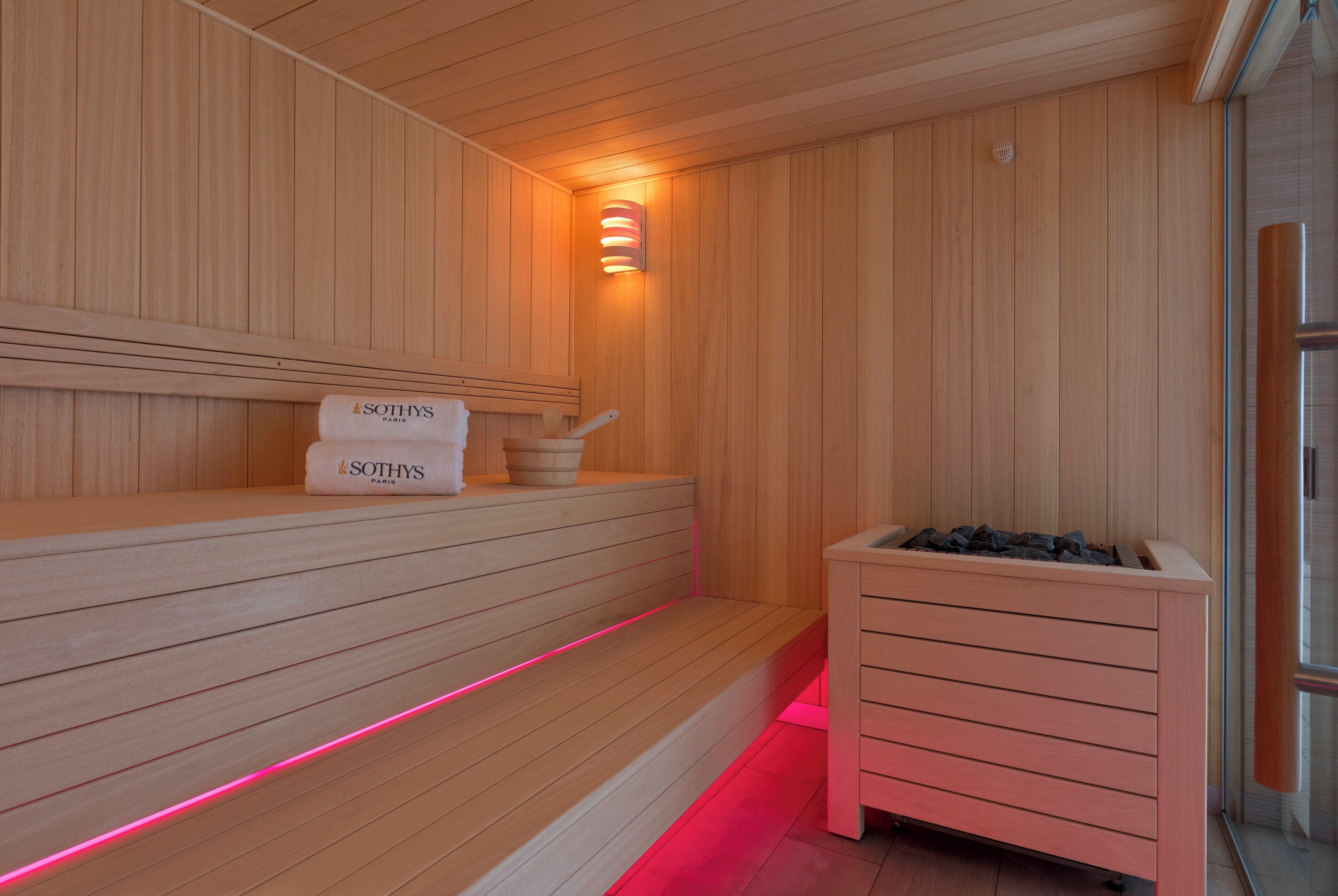 Una sauna de madera con bancos, un banco con una toalla y un calentador.