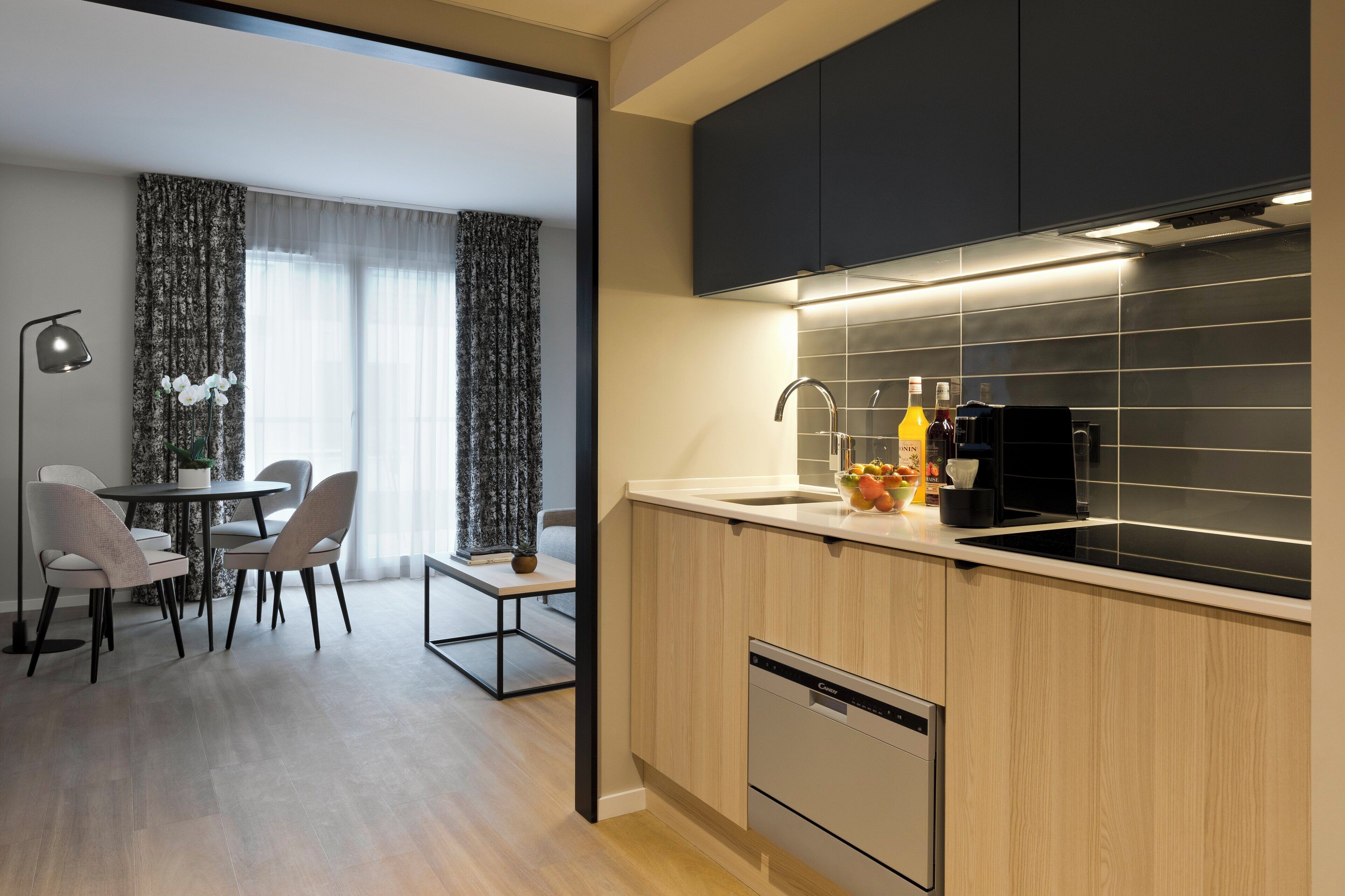 A modern kitchen with a dishwasher, a sink, and a coffee machine. There is a dining area with a table and chairs.
