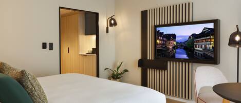 A modern hotel room with a large bed, a dining area, and a television displaying a cityscape.