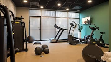 A gym with exercise equipment, a treadmill, and a large window with blinds.