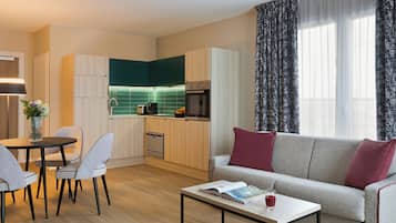 En kompakt opholdsstue med et tekøkken, et spiseområde og en sofa med puder.
