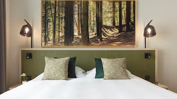 A hotel room with a large bed, two pillows, a nightstand, a wall-mounted painting of a forest, and two bedside lamps.
