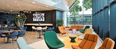 A modern lounge area with multiple seating options, including chairs and sofas, and a large window providing a view of the outdoors.