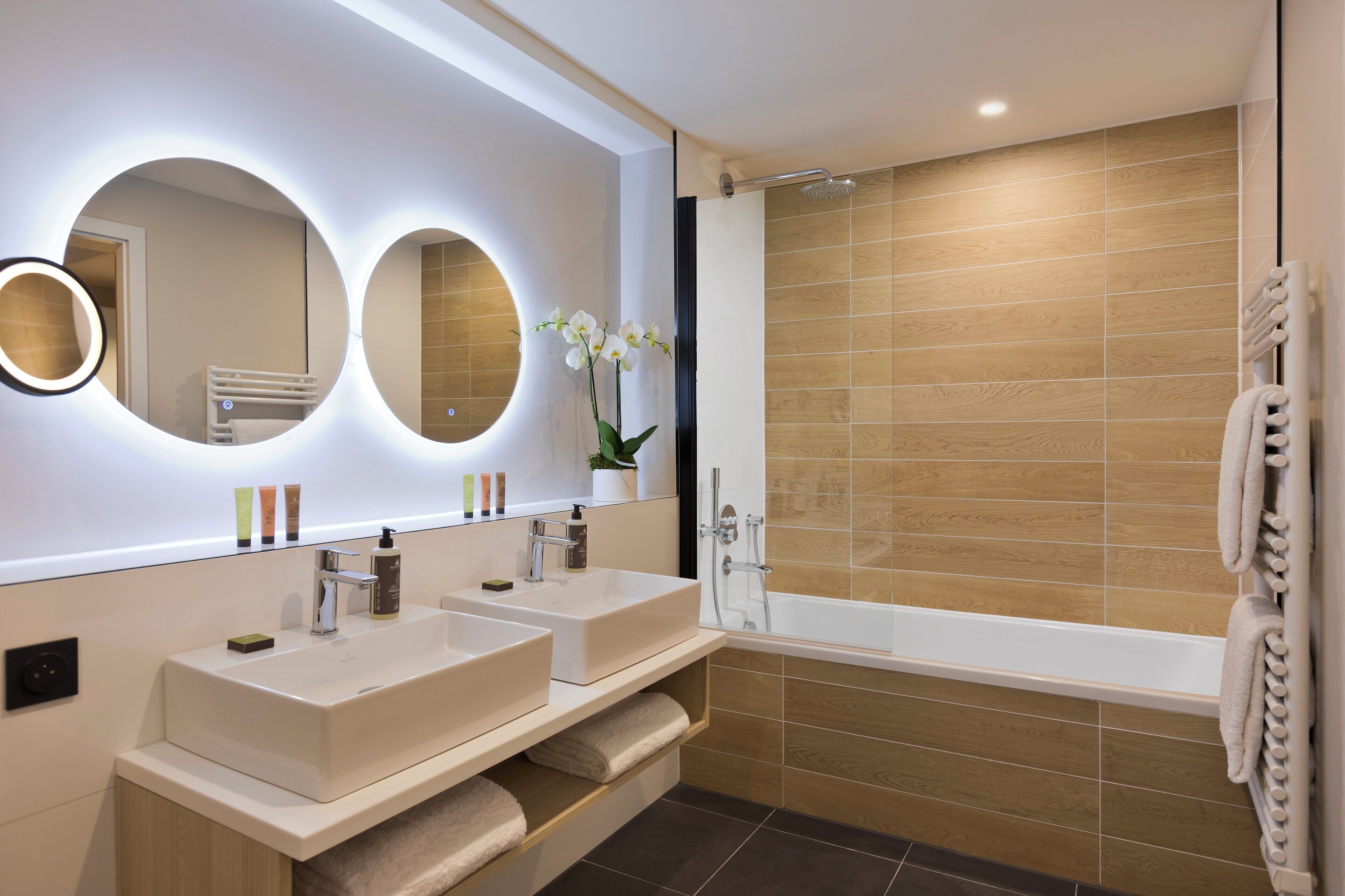 A modern bathroom with two sinks, a large mirror, and a shower.