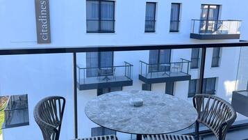 Un balcón con una mesa redonda y cuatro sillas de mimbre, con vistas a un edificio con varias ventanas y un letrero que dice 'citadines'.