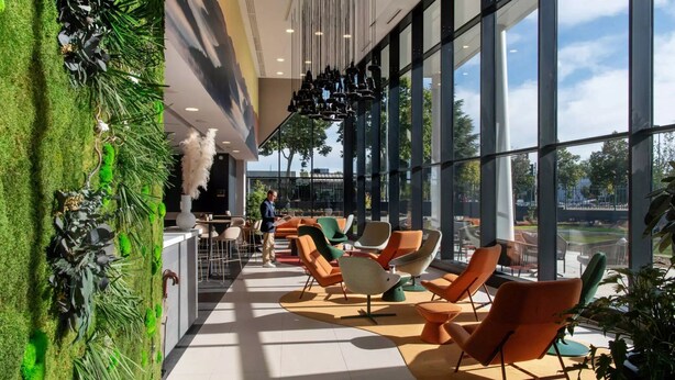 Un espacio interior amplio con ventanas grandes, asientos modernos y una pared verde con plantas.