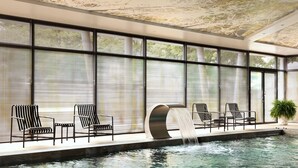 Zona de piscina con una cascada, sillas de descanso y ventanas amplias.