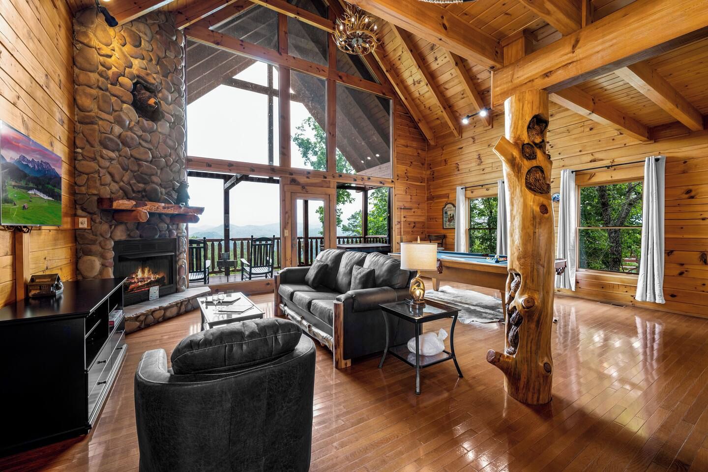 L’intérieur d’une cabane en rondins, avec une cheminée en pierre, une table de billard, des meubles en cuir et de grandes fenêtres.