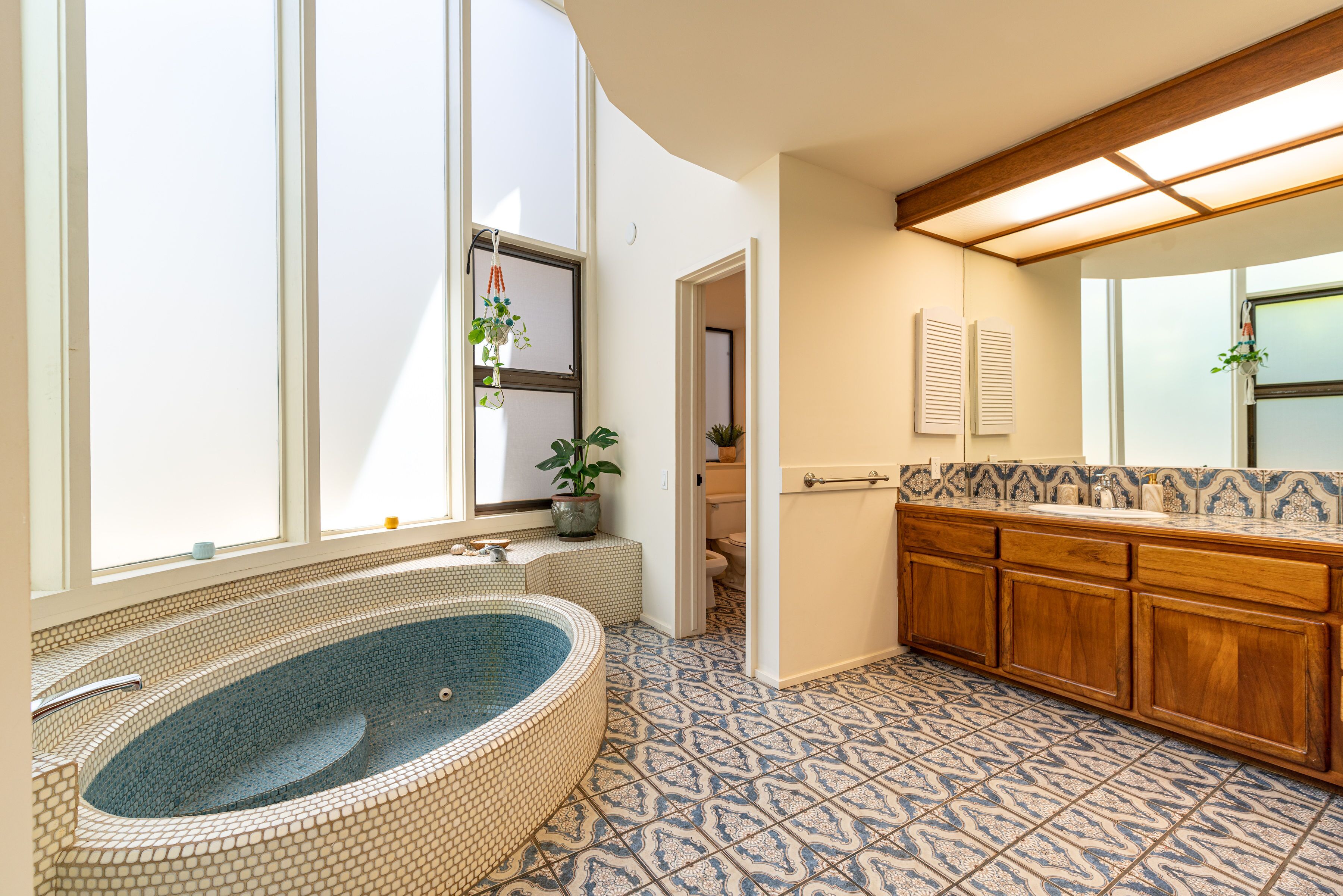 A bathroom with a large bathtub, wooden cabinets, and patterned floor tiles.