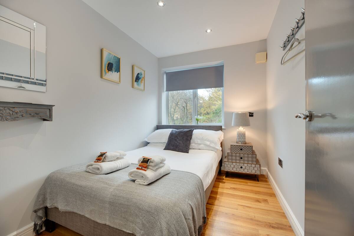 A neatly made bed with towels, a bedside lamp, and a window with a view of trees.