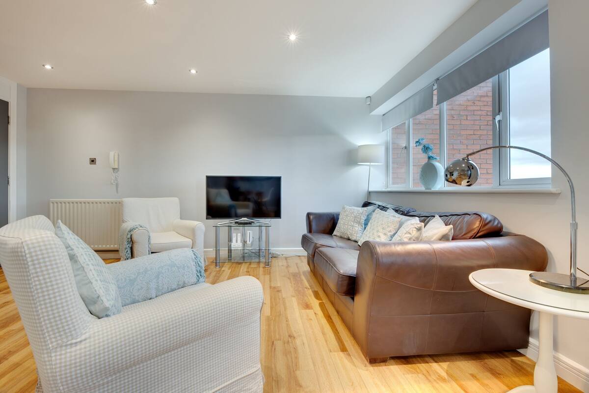 A modern living room with a flat-screen TV, two sofas, a coffee table, and a window with a view of a brick building.