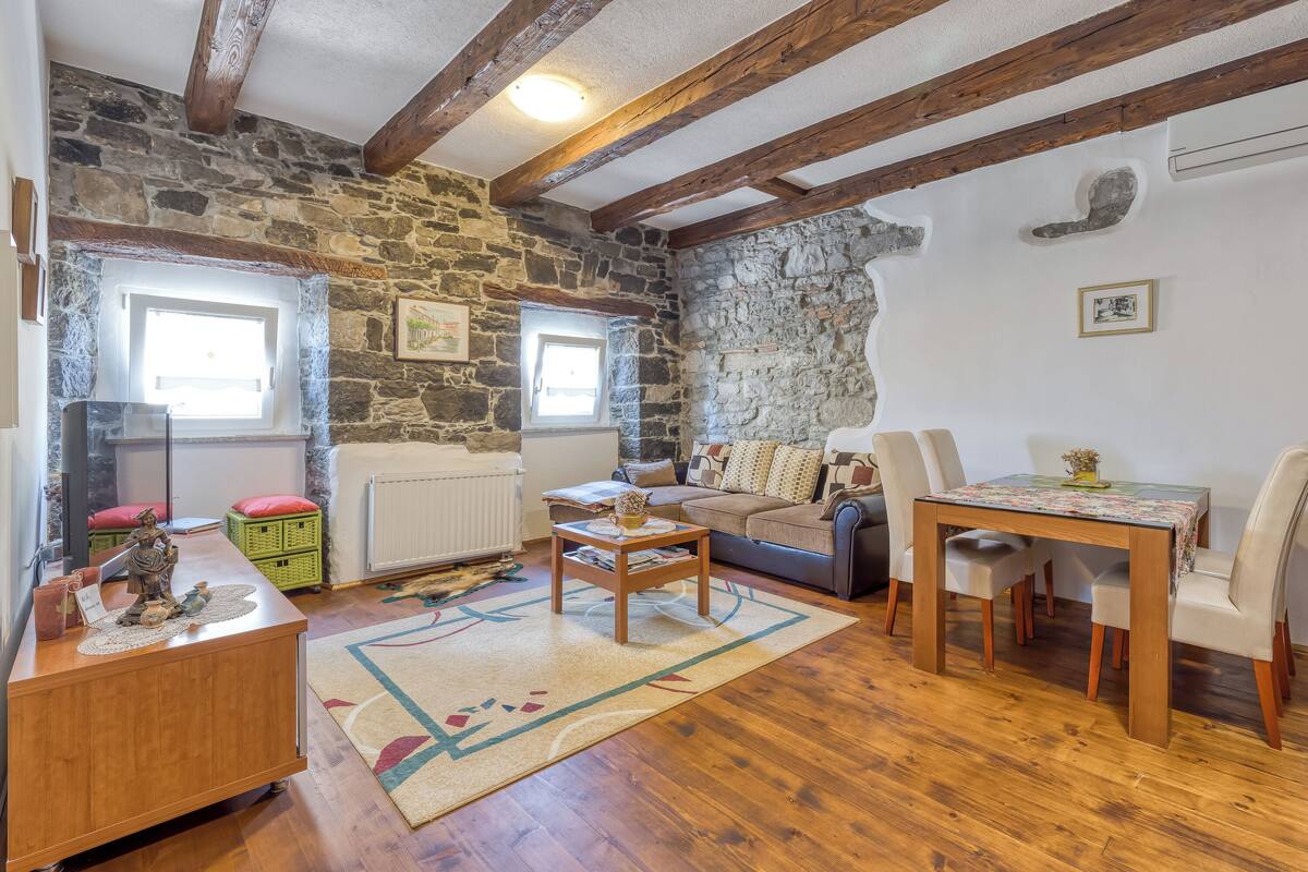 Ein gemütliches Zimmer mit Steinwänden, Holzbalken, einer Couch, einem Tisch und einer Heizung.