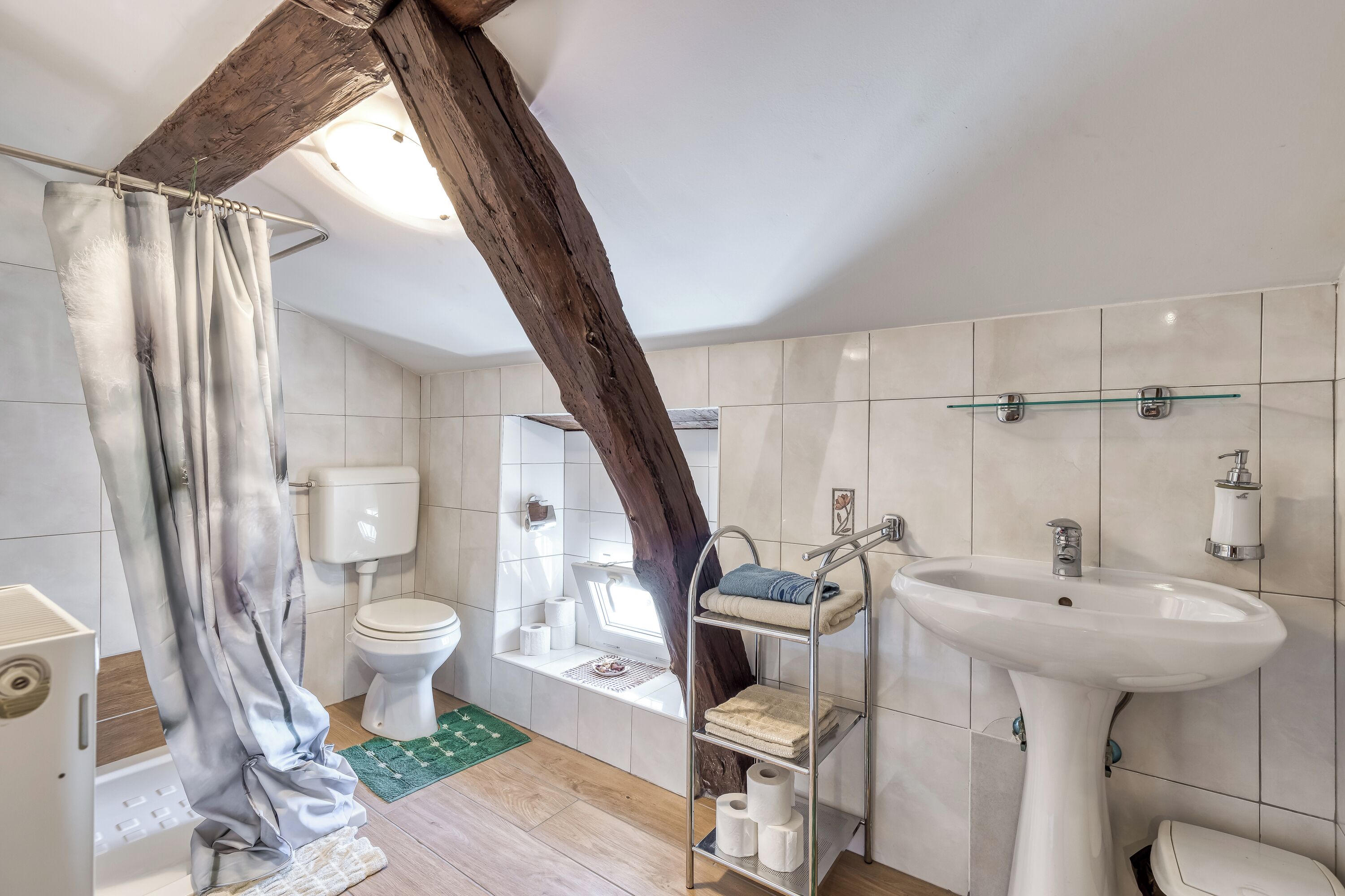 A bathroom with a toilet, sink, shower, and a shelf with towels.