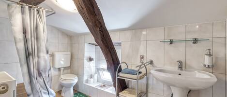 A bathroom with a toilet, sink, shower, and a shelf with towels.