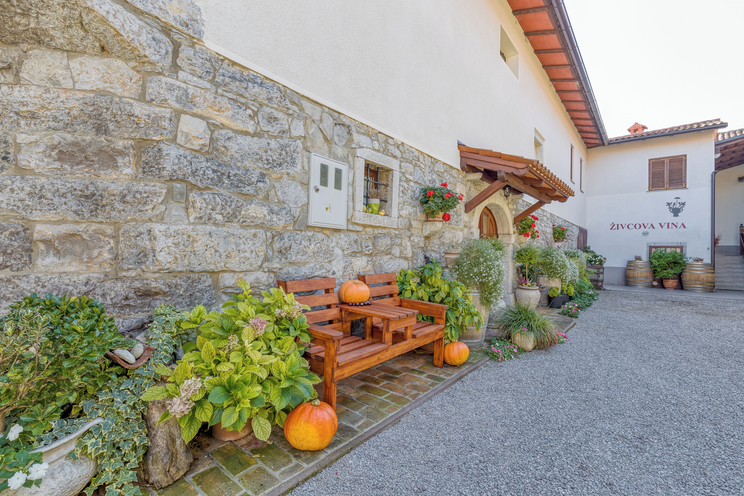 A stone building with a wooden bench, potted plants, and barrels.