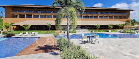Un hotel con piscina, mobiliario de exterior y un edificio grande con varios balcones.