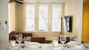 Ein Essbereich mit Tisch für vier Personen, einem braunen Sofa und einem Fenster mit Jalousien.