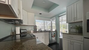 A modern kitchen with white cabinets, a granite countertop, and a window providing natural light. - Family Home w/Pool , On Golf Course & Near Beach !  (Fort Myers)