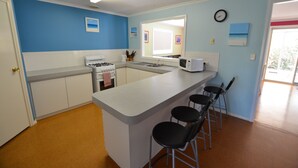 A kitchen with a central island, white cabinets, a stove, a microwave, and three bar stools.