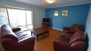 A living room with a brown leather sofa, a wooden coffee table, and a television on a stand.