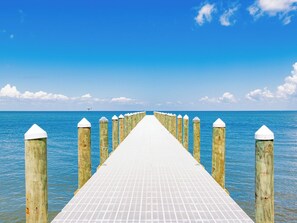 Une longue jetée s’étendant dans des eaux calmes et bleues, sous un ciel dégagé.