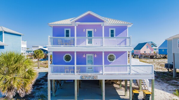Une maison de plage à deux étages avec un balcon, une enseigne indiquant « Coastal Caboose », et une plage de sable en arrière-plan.