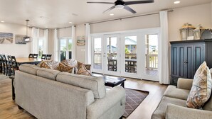 A spacious living room with a large sofa, a dining area with chairs, and a ceiling fan. - Steps to Beach | Pet Friendly | Community Pools and Pier (Gulf Shores)