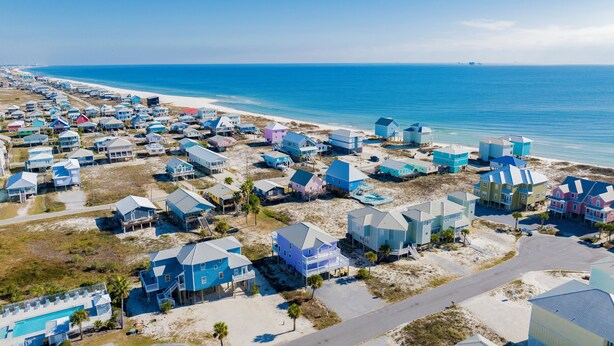 An aerial view of a coastal residential area with houses built on stilts over the beach, featuring a clear view of the ocean and sandy terrain. - Steps to Beach | Pet Friendly | Community Pools and Pier (Gulf Shores)