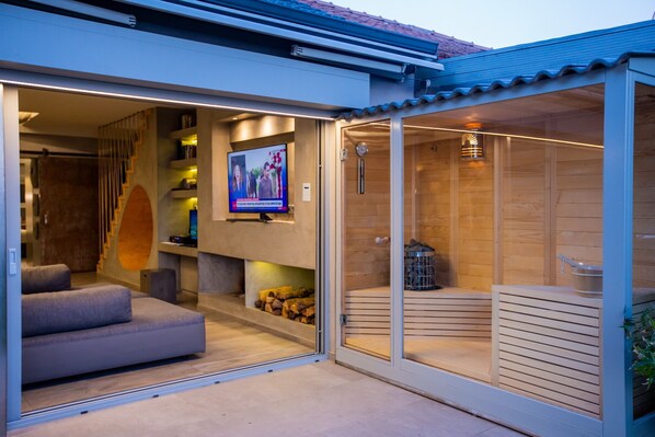A modern interior with a television mounted on a wall, a sofa, and a wooden sauna area. - Spa Villa Skaloma (Nafpaktos)