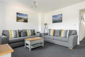 Een moderne woonkamer met twee grijze banken, een houten salontafel en een vloerlamp.