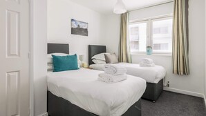 Une chambre d’hôtel avec deux lits, une fenêtre avec des rideaux, un tableau au mur et une porte blanche.
