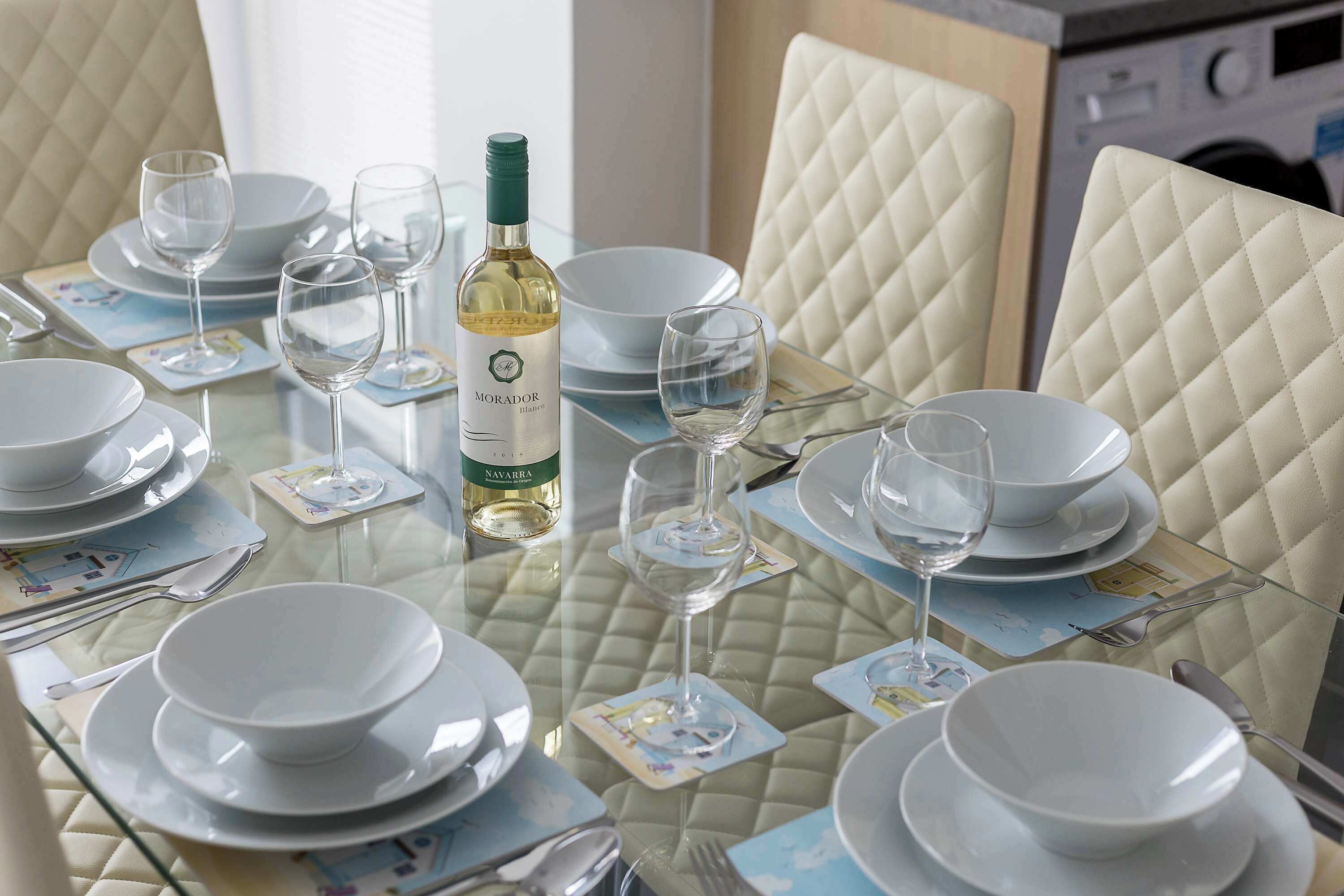 Een eettafel gedekt met witte borden, kommen en wijnglazen, een fles wijn en een menukaart.