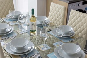 Une table à manger dressée avec de l’assiette blanche, des bols et des verres à vin, une bouteille de vin et un menu.