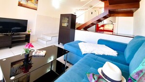 A modern living room with a blue sofa, a flat-screen TV, a coffee table, and a staircase leading to an upper level. - El cortijo, pool view (Costa Adeje)