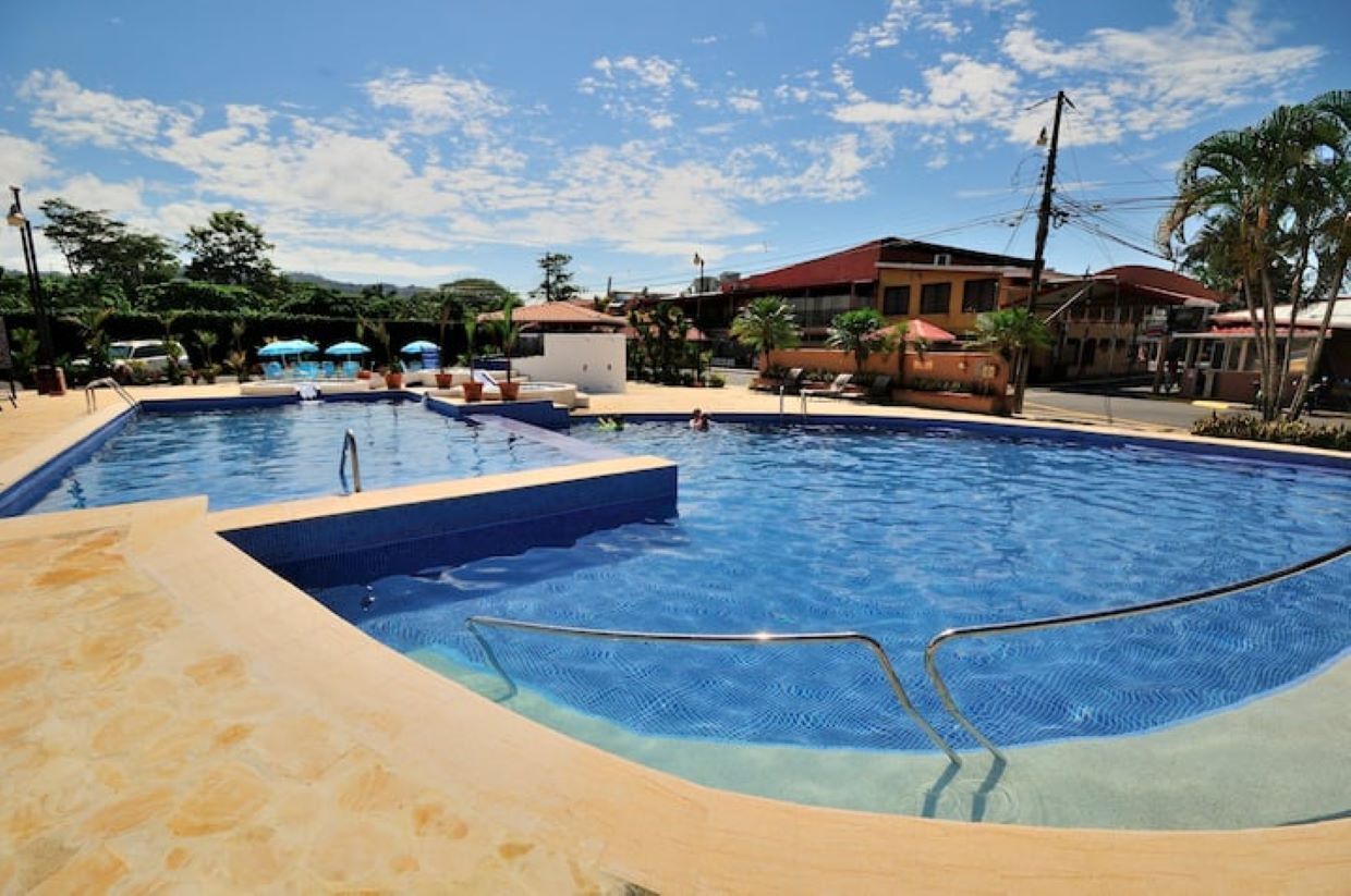 Una piscina con agua cristalina y azul, rodeada de sillas de descanso y sombrillas.