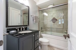 A bathroom with a black vanity, a white toilet, a glass-enclosed shower, and a large mirror.