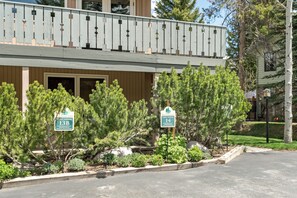 A two-story building with a balcony, surrounded by evergreen trees and a landscaped garden.