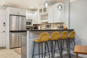 A kitchen with white cabinets, a stainless steel refrigerator, a coffee maker, and a bar stool area. - Ski Condo in Vail Village (Vail)