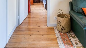 A hallway with wooden flooring, a green sofa, a woven basket, and a painting on the wall.