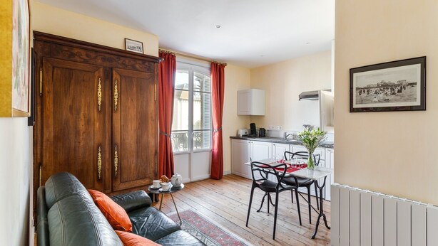 A compact living space with a sofa, a dining table with chairs, a kitchen area with a coffee machine, and a radiator.