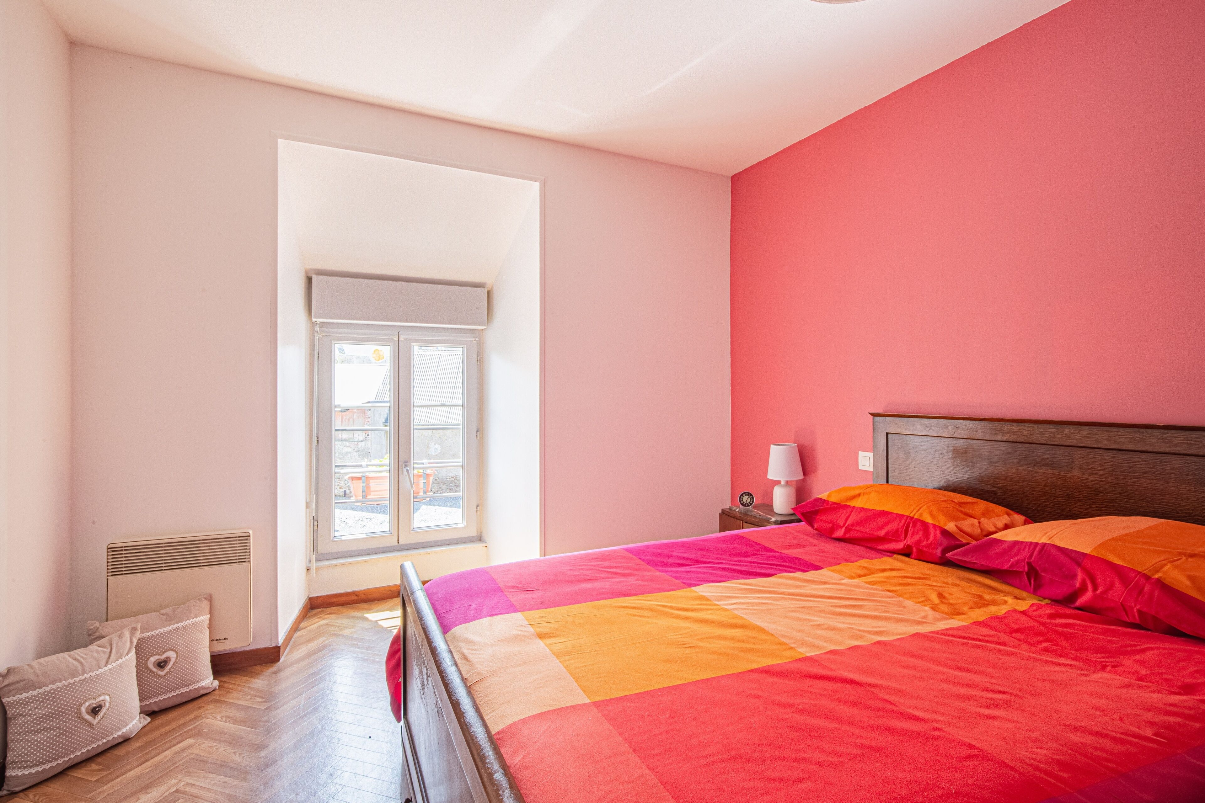 Een slaapkamer met een bed, nachtkastje, raam en radiator.
