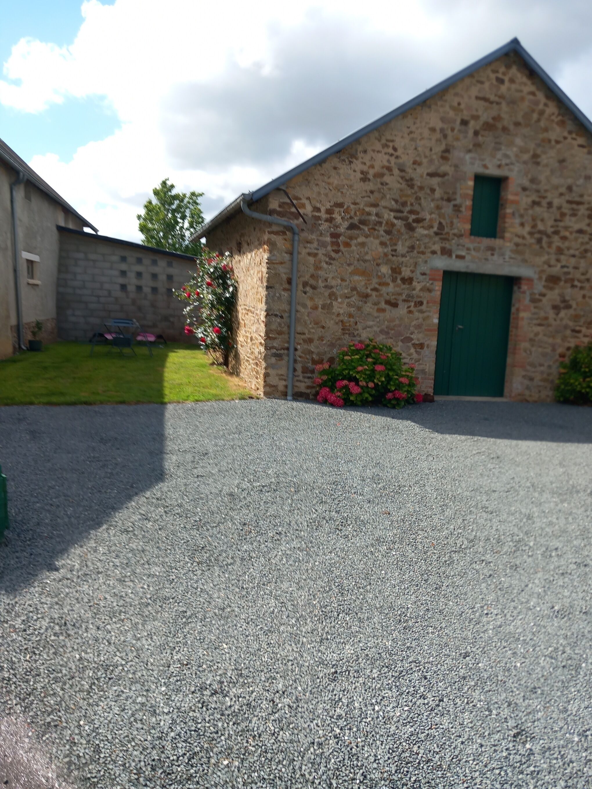 Un bâtiment en pierre avec une porte verte, une allée pavée et une pelouse agrémentée de fleurs.
