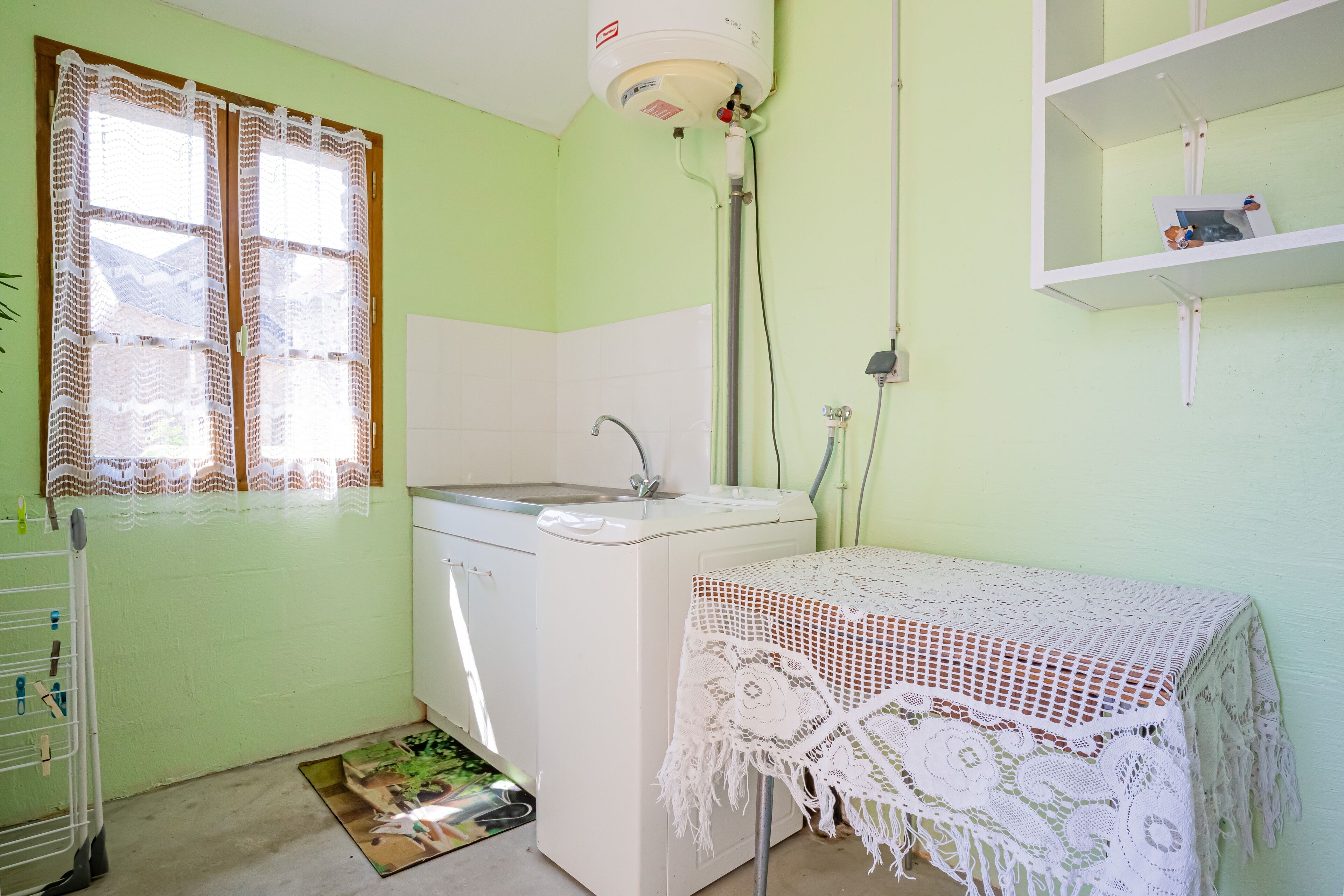 A small laundry room with a washing machine, a sink, and a table covered with a white lace tablecloth.