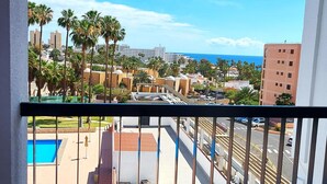 A balcony with a view of a swimming pool, palm trees, and a cityscape with buildings and the ocean. - Viña del Mar, ocean view (Costa Adeje)