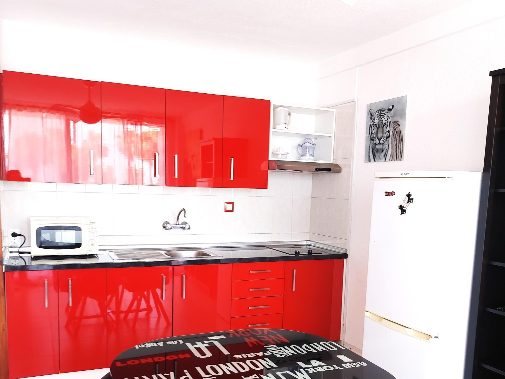 Een kleine keuken met rode kastjes, een witte magnetron en een zwart aanrecht.