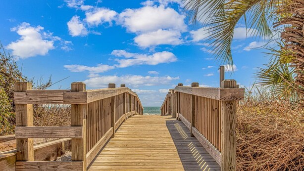 A wooden boardwalk leading to the beach with a clear sky and palm trees. - Long Bay Dunes A3-Oceanfront Condo in Myrtle Beach (Myrtle Beach)