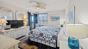 A hotel room with a bed, a television, a desk, a chair, a ceiling fan, and a window with curtains. - Long Bay Dunes A3-Oceanfront Condo in Myrtle Beach (Myrtle Beach)