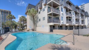 A swimming pool with a poolside area, a multi-story building with balconies, and palm trees. - Long Bay Dunes A3-Oceanfront Condo in Myrtle Beach (Myrtle Beach)