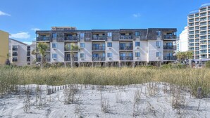 A multi-story building with balconies, located near a sandy beach with vegetation. - Long Bay Dunes A3-Oceanfront Condo in Myrtle Beach (Myrtle Beach)