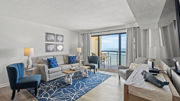 A modern living room with a sofa, armchairs, a coffee table, and a view of the ocean through large windows. - Oceans 914 -Oceanfront 2BR- Accommodates 8 (North Myrtle Beach)